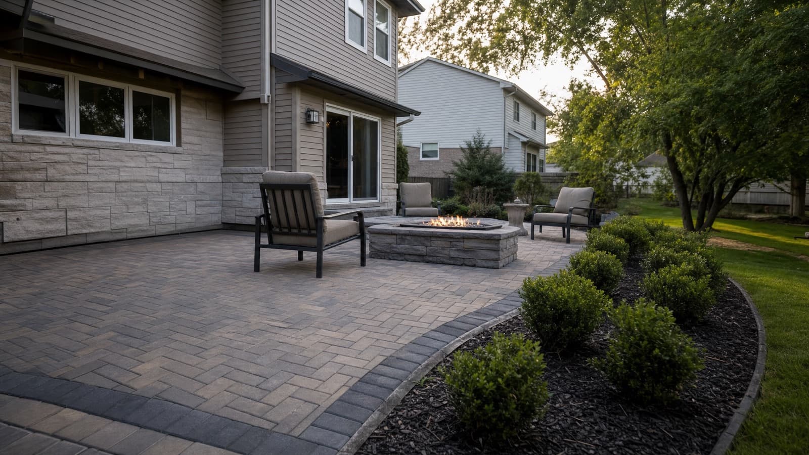 Newly installed herringbone paver patio with fire pit behind a suburban Will County, IL home