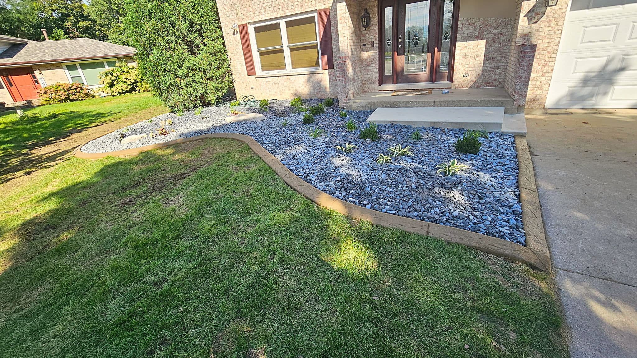 Stamped concrete curbing curving around a blue-gray rock bed at the front of a brick home
