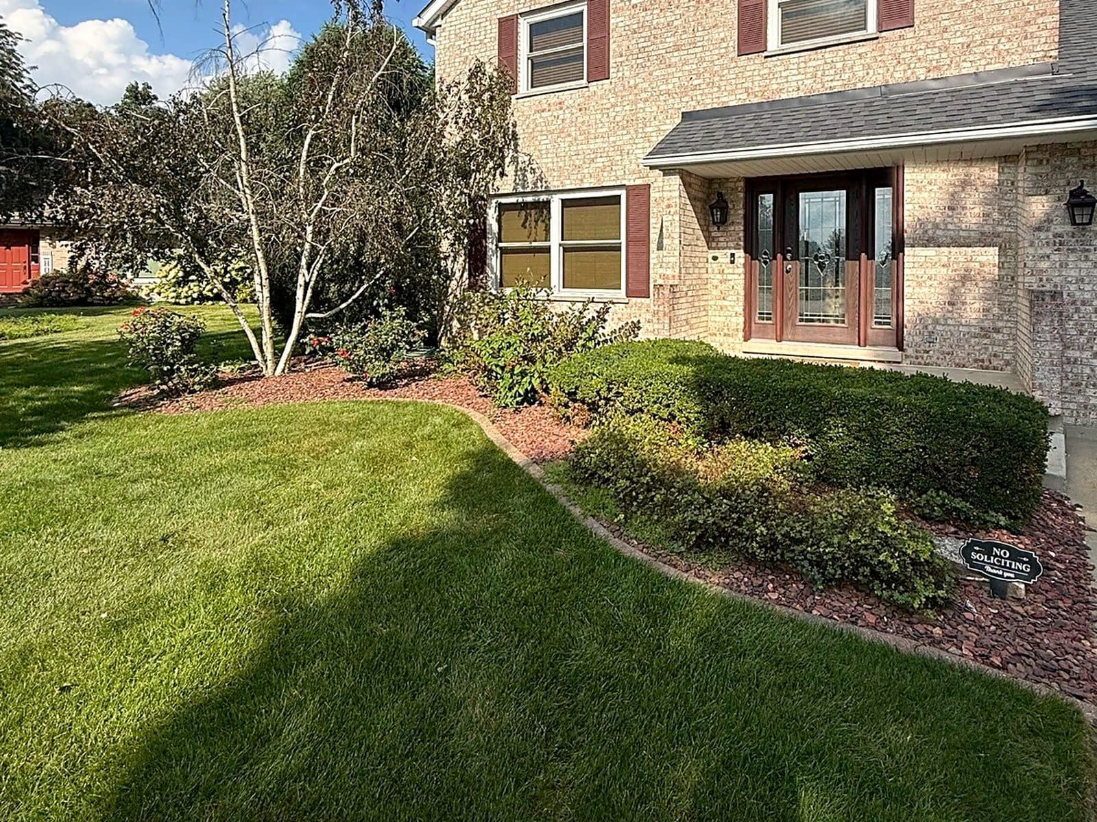 Before: front yard with overgrown bushes and red rock, redone with stamped concrete curbing and blue-gray rock