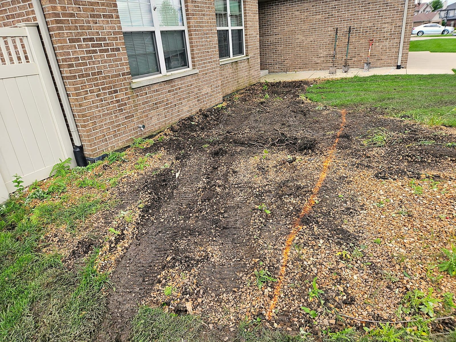 Before: bare, torn-out bed along a brick house, finished with river rock, a new tree and concrete curb edging
