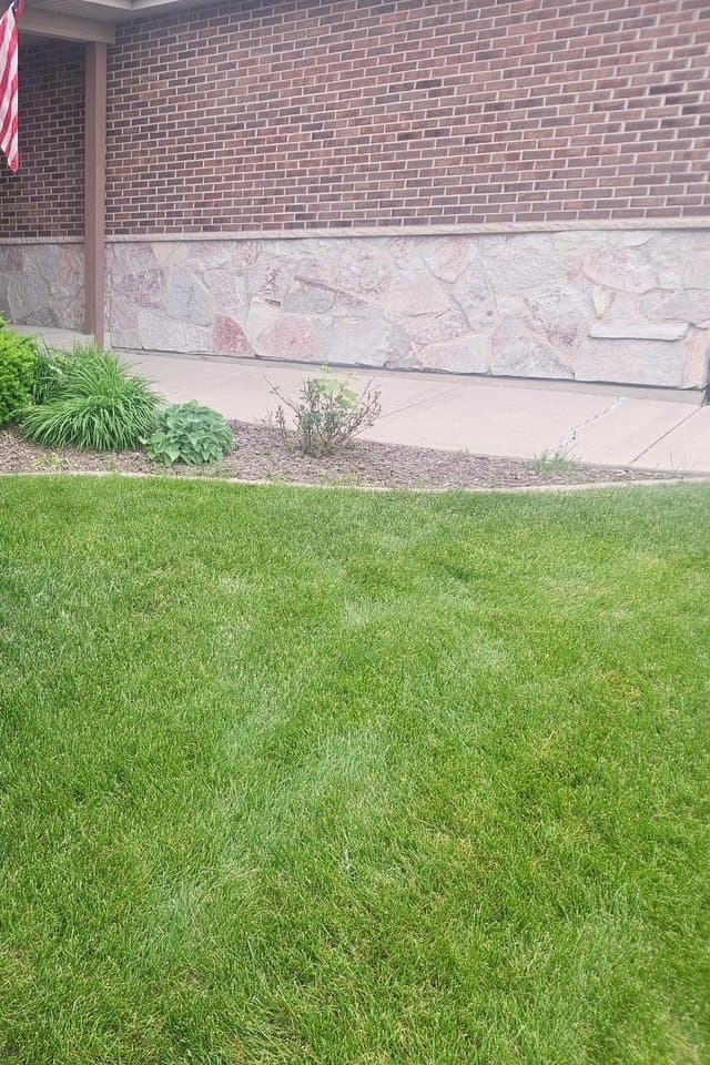 Brick home with trimmed porch shrubs, fresh mulch, and healthy green lawn