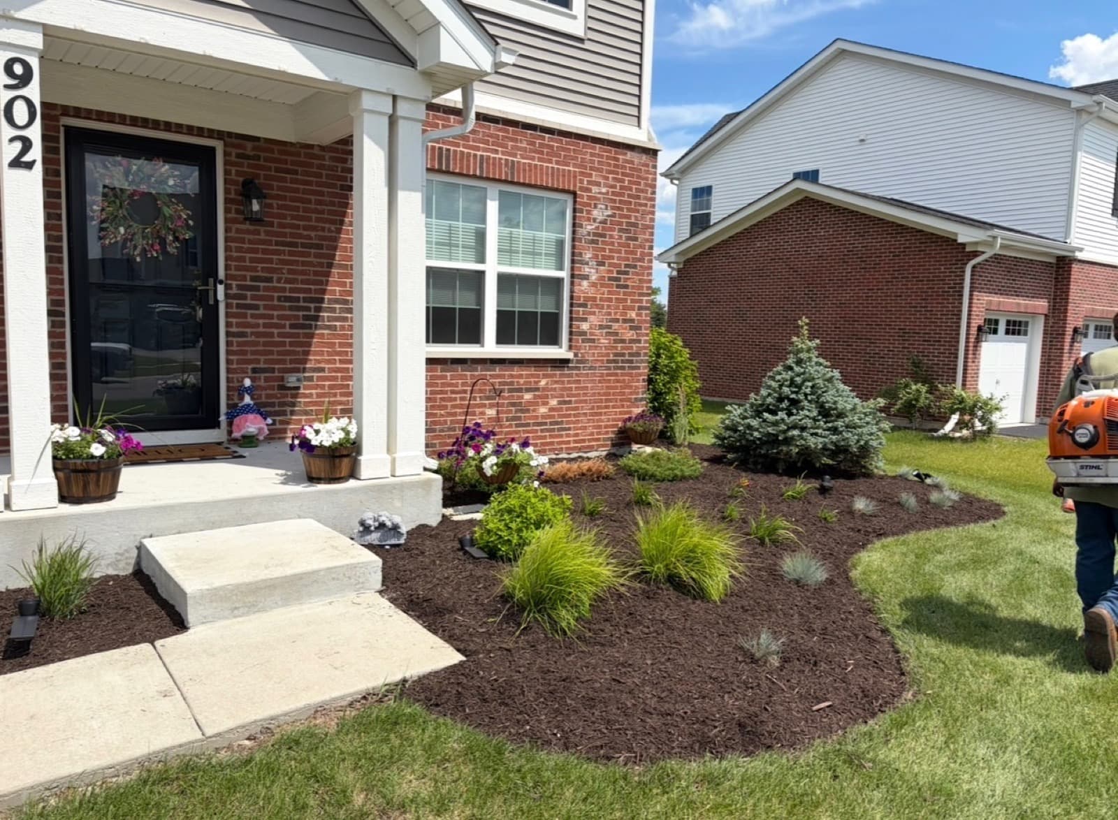 Freshly installed landscape bed with new plantings, ornamental grasses, and dark mulch at a brick home entry