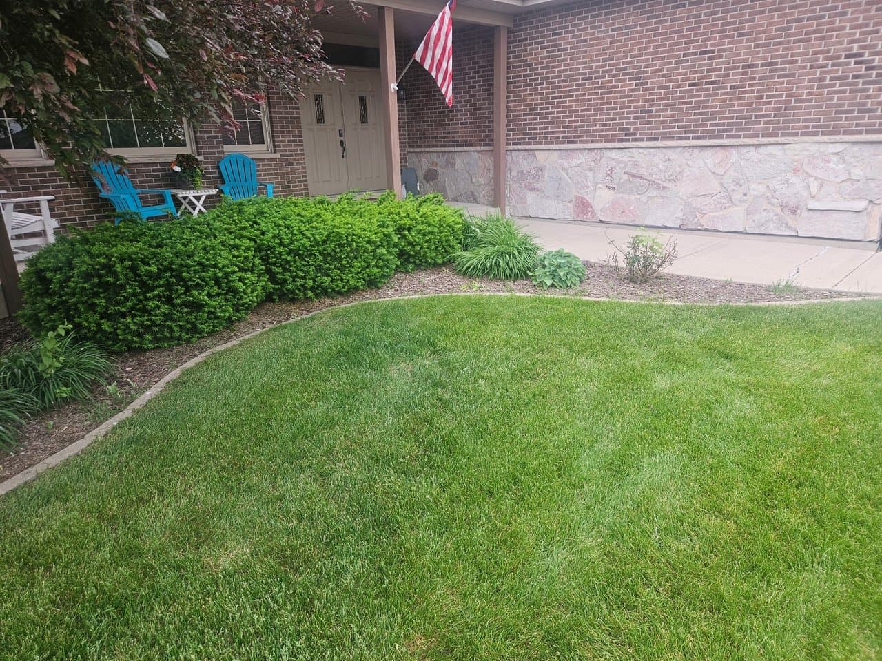 Brick home entry with trimmed porch shrubs, fresh mulch, and healthy green lawn